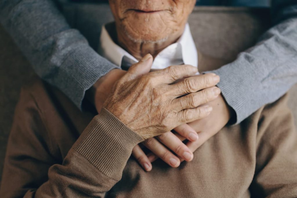 Senior with Alzheimer's sitting in chair with family member hugging from behind
