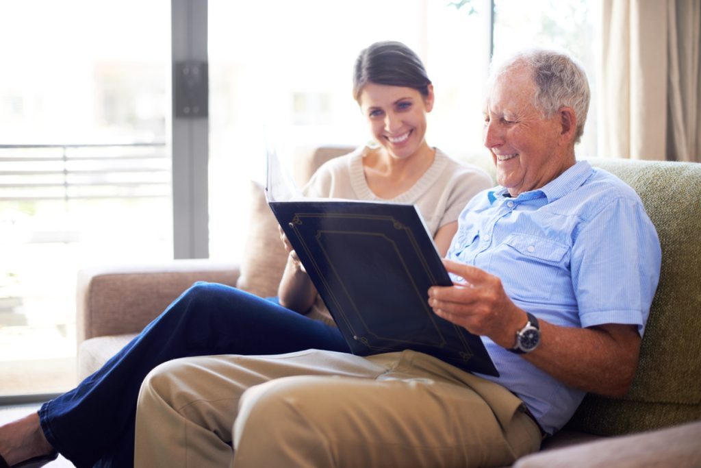 Memory care resident sitting with younger relative volunteer looking at family photos