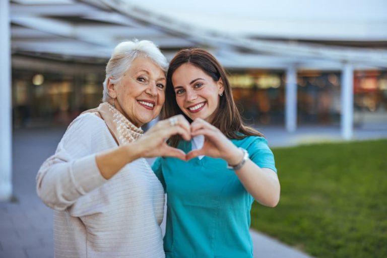 Elderly person and caregiver form heart shape with their hands outside