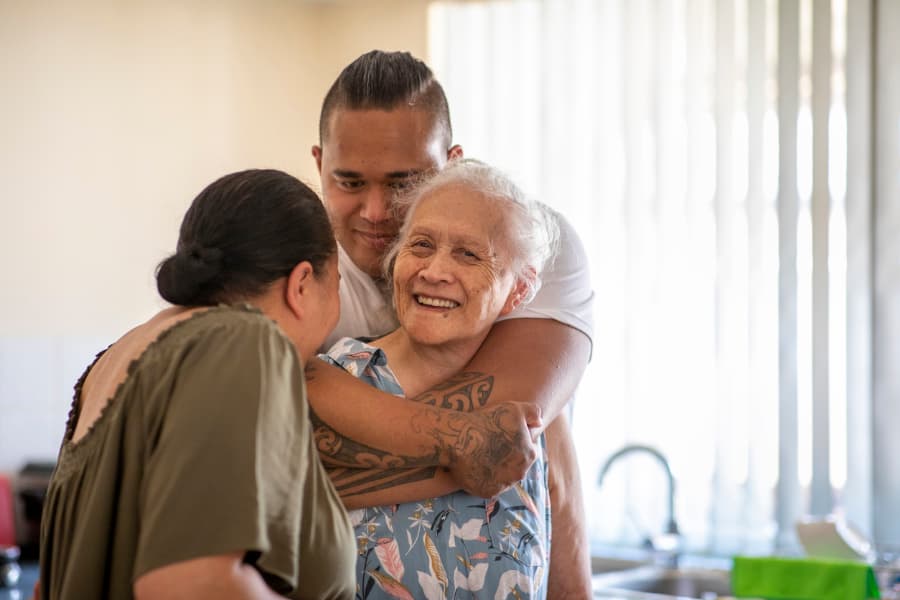 Senior person with relatives cuddling each other in kitchen at home