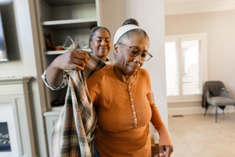 Caregiver helping to dress senior