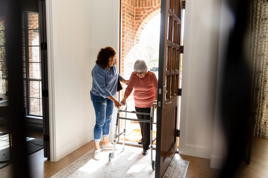 Healthcare worker helps an elderly resident into house