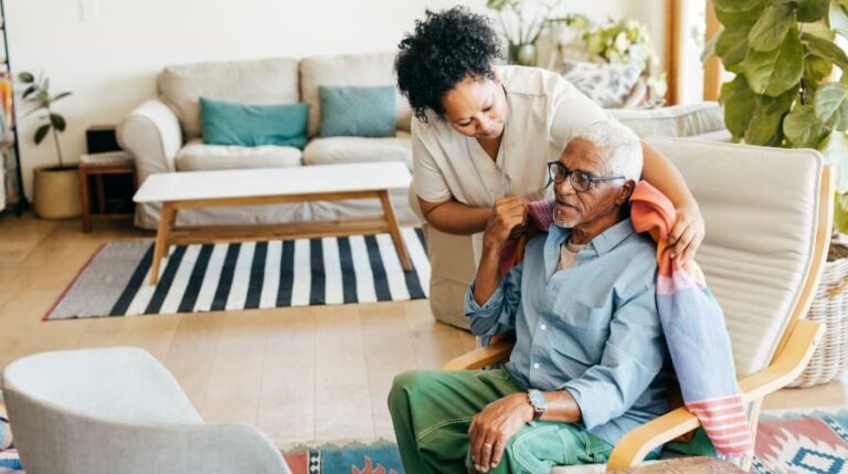 Caregiver at home putting blanket around older individual