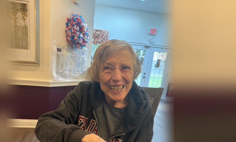 A smiling Fox Trail memory care resident seated at her dining table in one of our homes
