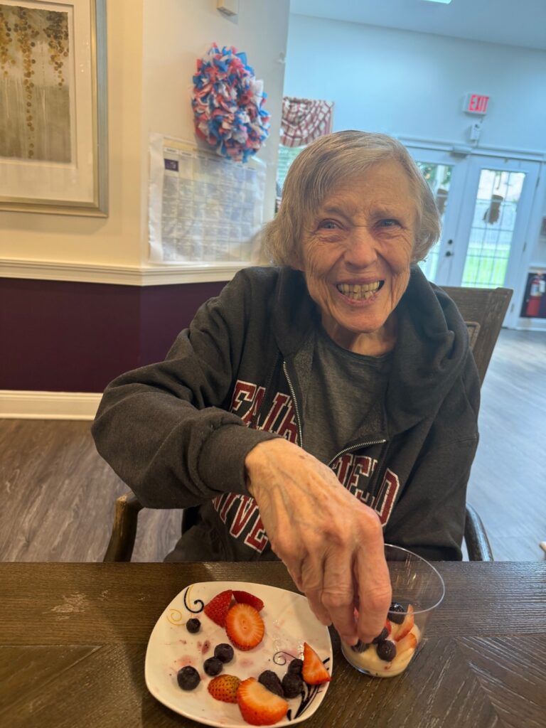 A smiling Fox Trail memory care resident enjoying a plate of fresh strawberries and blueberries at her dining table
