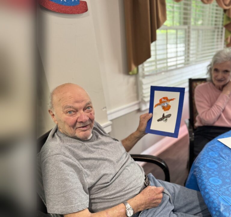 A Fox Trail memory care resident smiling as he holds up a painting he made during an art activity