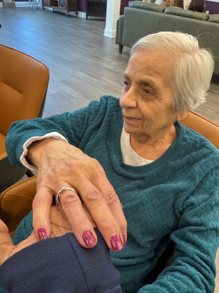 A Fox Trail memory care resident sitting in a lounge chair after having her nails painted, her hand resting in a caregiver's hand